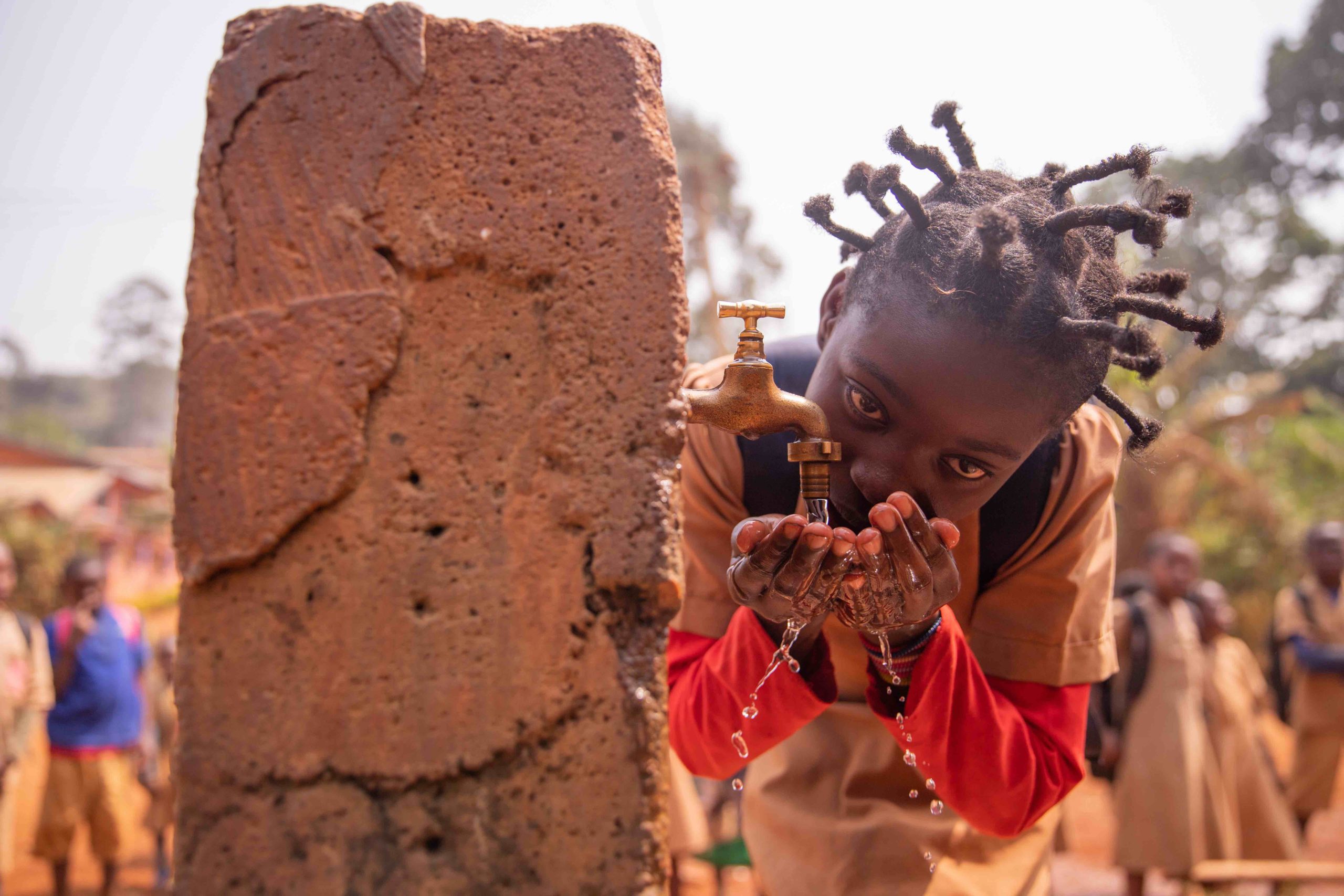 bambina in villaggio africano Fotografia di una bambina che si abbevera con le mani in una fontanella in un villaggio africano
